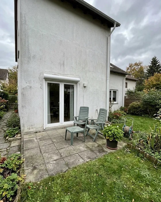 Hauswand mit Terrassentür und Terrasse ohne Dach, davor zwei Gartenstühle